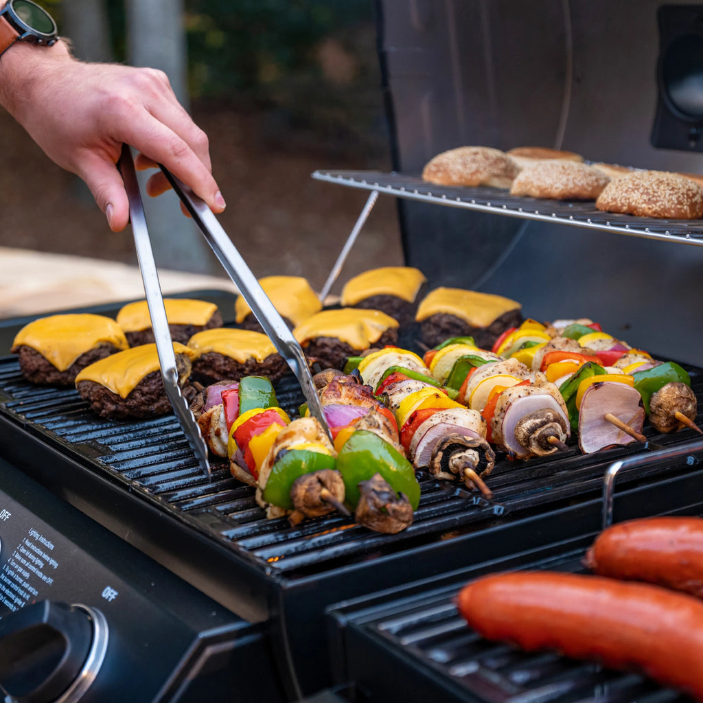 Cheeseburgers and skewers roasting on the gas side of the grill. Sausages cooking on the charcoal side can barely be seen to the right.