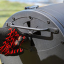 Someone wearing a heat-resistant glove opens the slide of the damper in the left side of the grill.