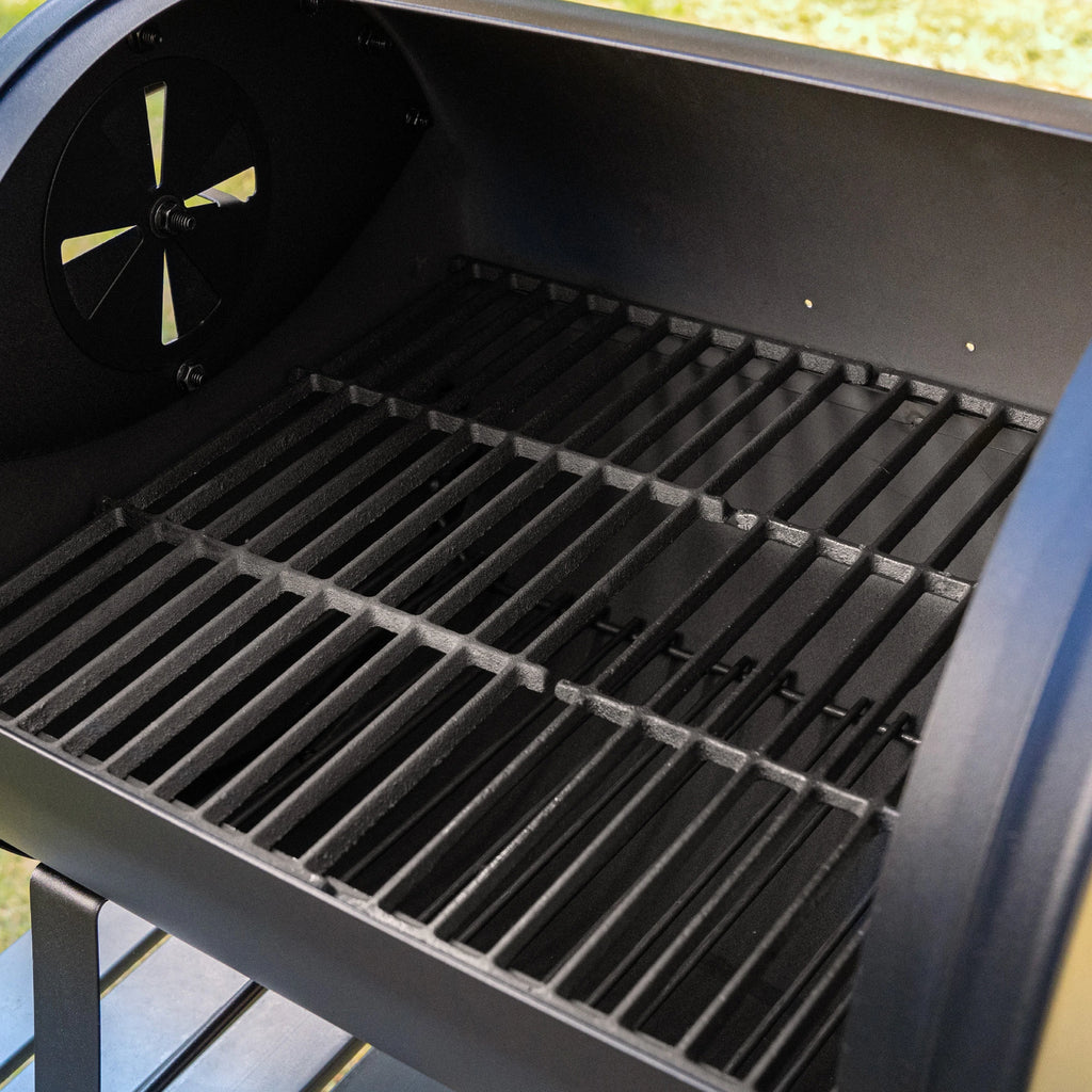Inside view of the tabletop grill with the lid open showing the cast iron cooking grate above a smaller metal fire grate. The left side damper is slightly open.